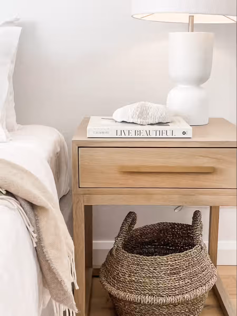 Coral and a ribbed lamp on the oak bedside table, a basket tucked beneath