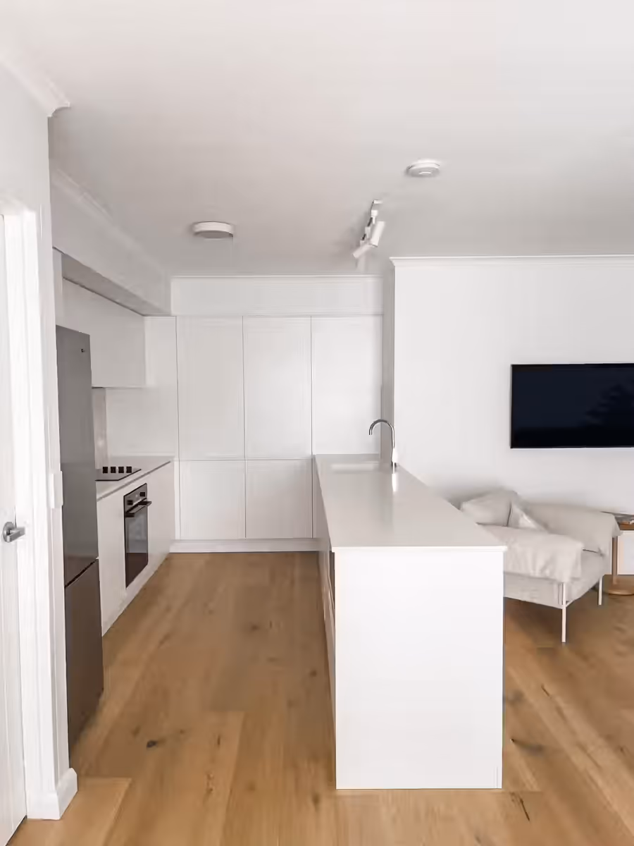 White galley kitchen and island bench, opening onto the living room