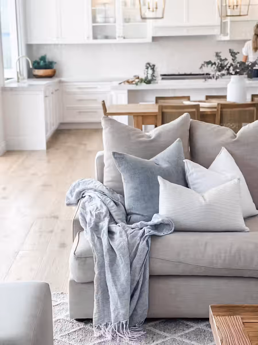 Grey sofa layered with blue cushions and a throw, the white kitchen beyond