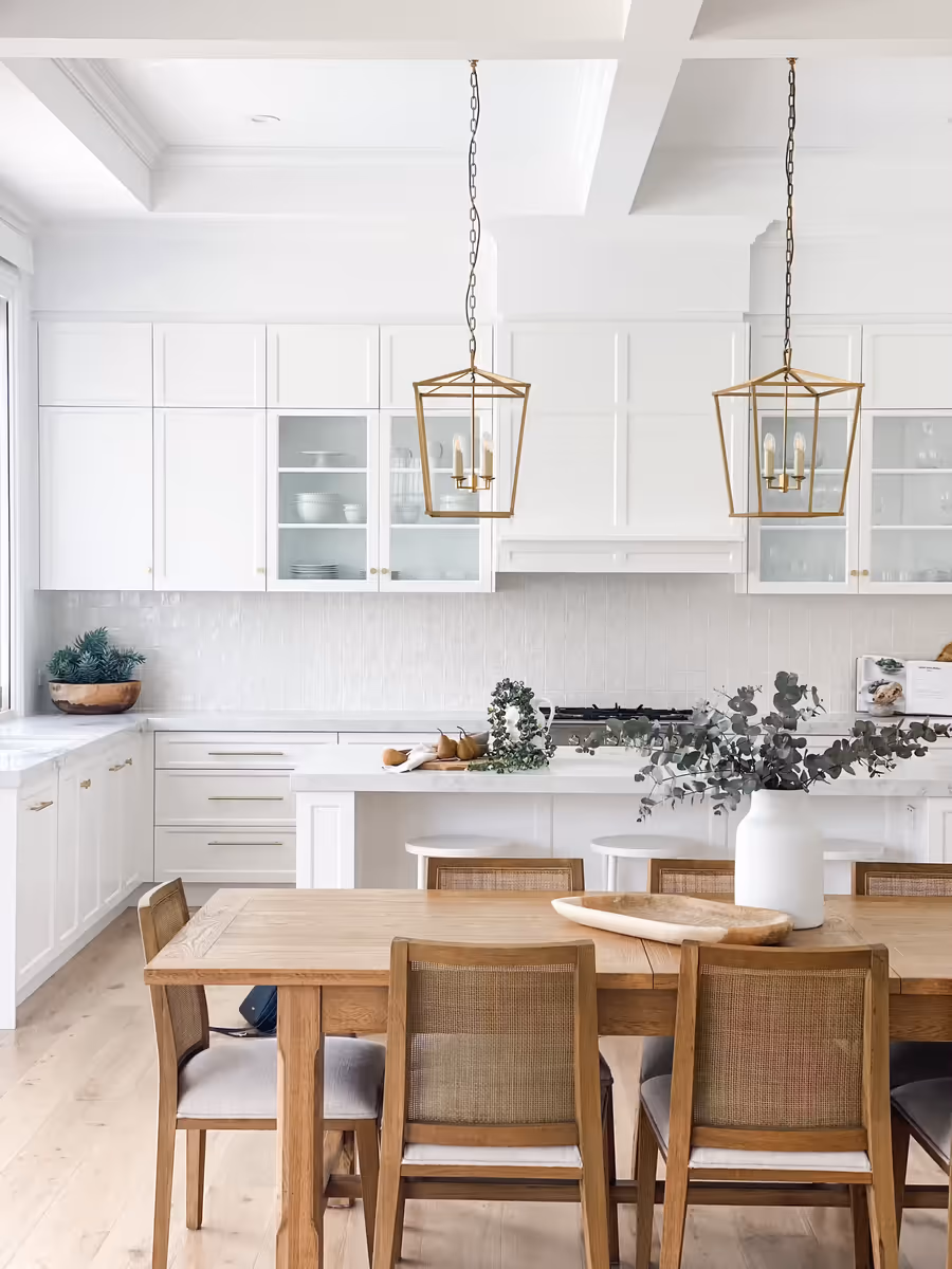 White shaker kitchen with brass lantern pendants above the island and a timber dining table