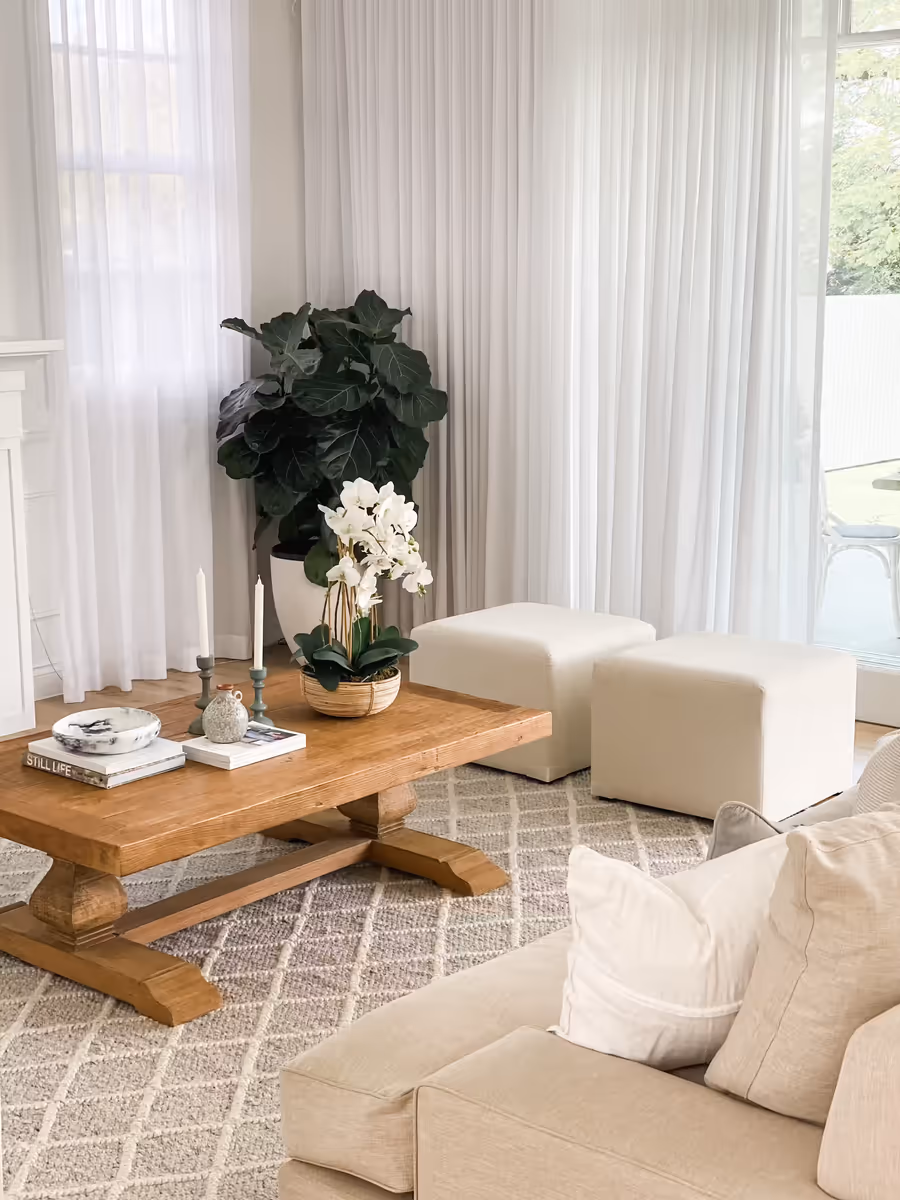 Trestle coffee table and white ottomans between linen sofas, sheers behind