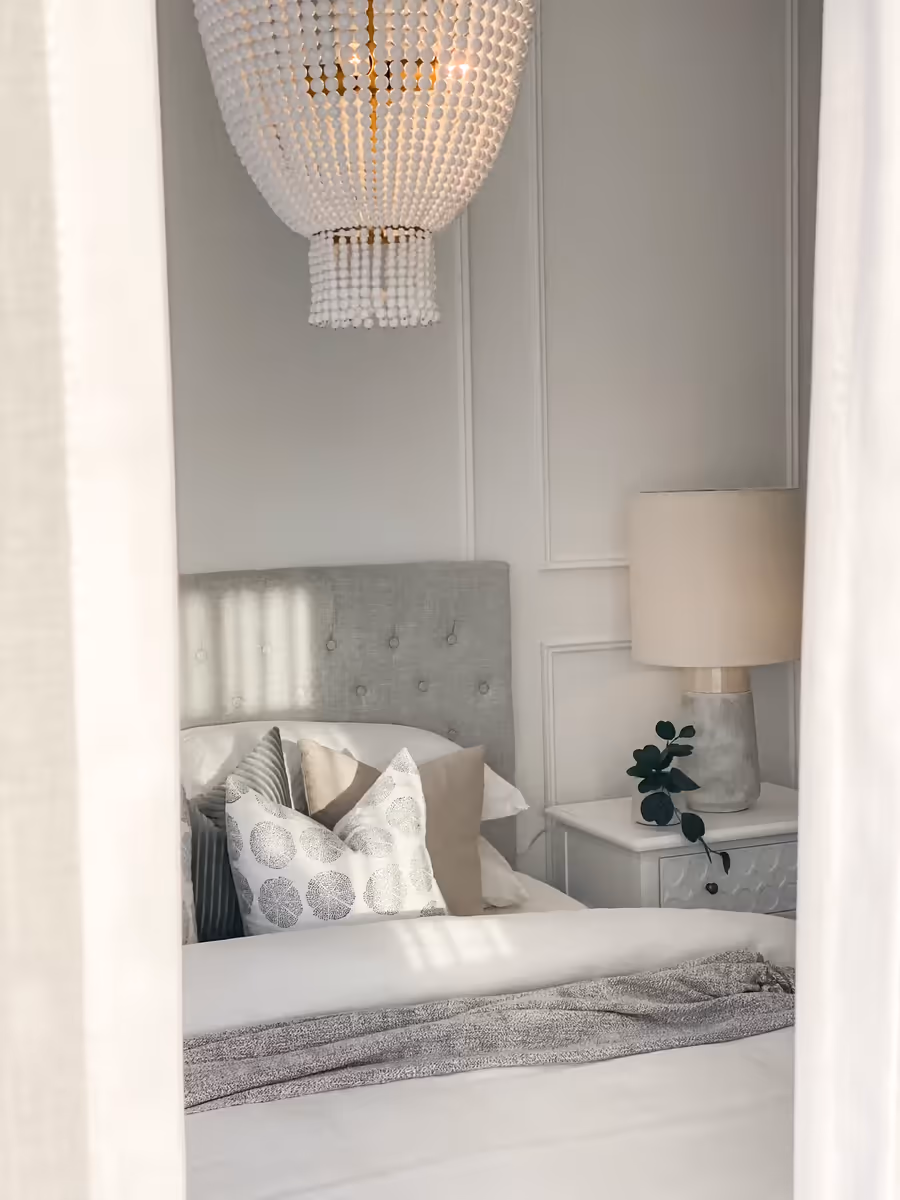Beaded chandelier above a buttoned bedhead, seen through sheer curtains