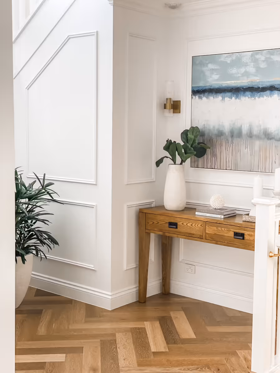 Timber console below a coastal canvas in the panelled entry, on herringbone floors