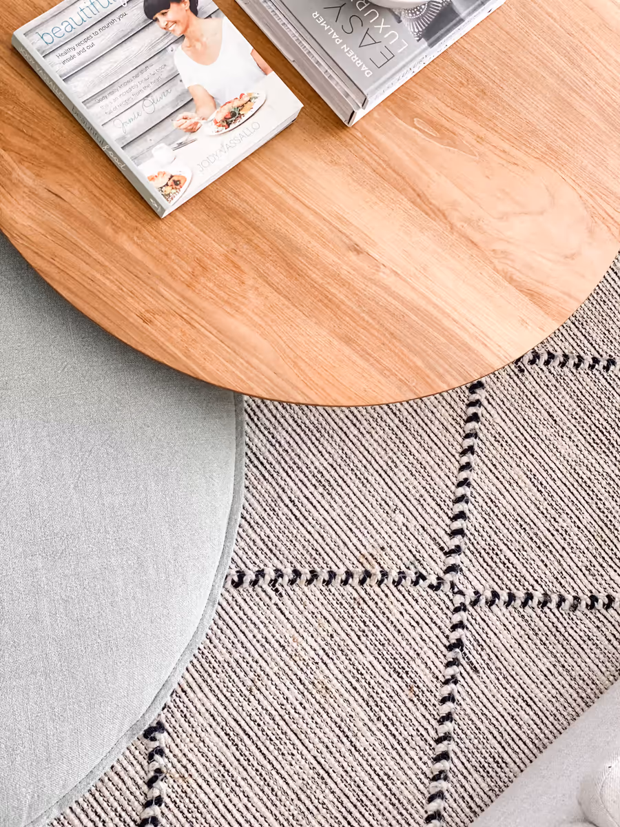 Round oak table overlapping a sage ottoman on a black-checked wool rug