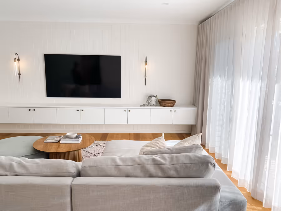 Panelled media wall with slim wall lights either side of the television, sheers drawn
