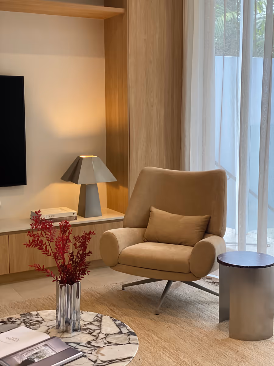 Tan swivel chair and a marble side table by the sheer curtains, lamp lit behind