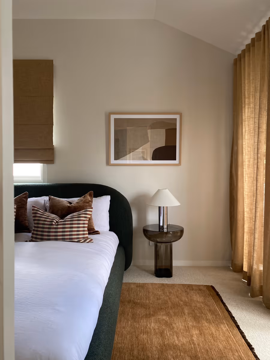 Dark green boucle bedhead with check cushions, beside a smoked glass bedside table