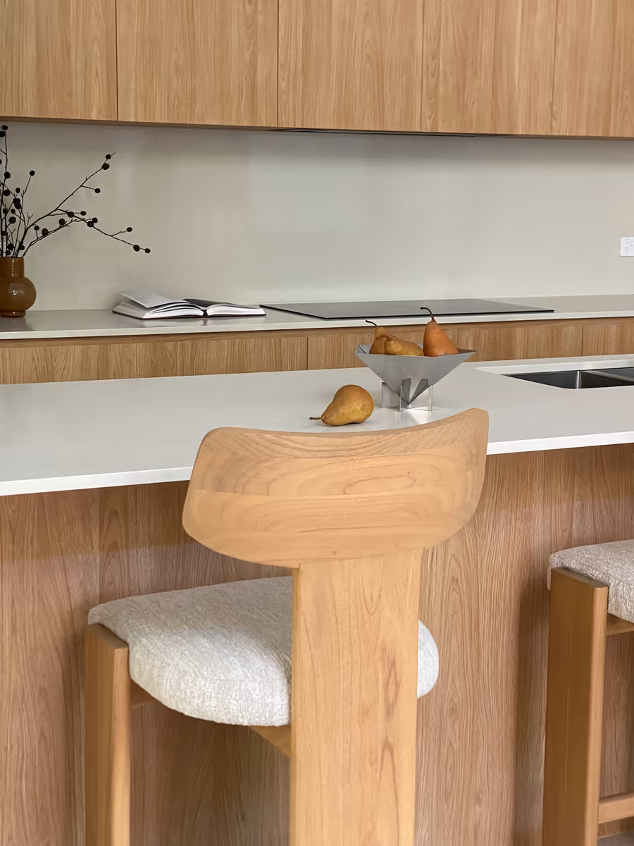 Sculptural oak bar stool at the kitchen bench, with pears in a metal bowl