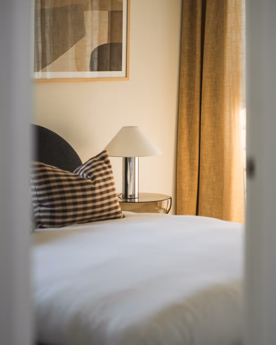 Check and rust cushions on white bedding, gold curtains drawn at the window