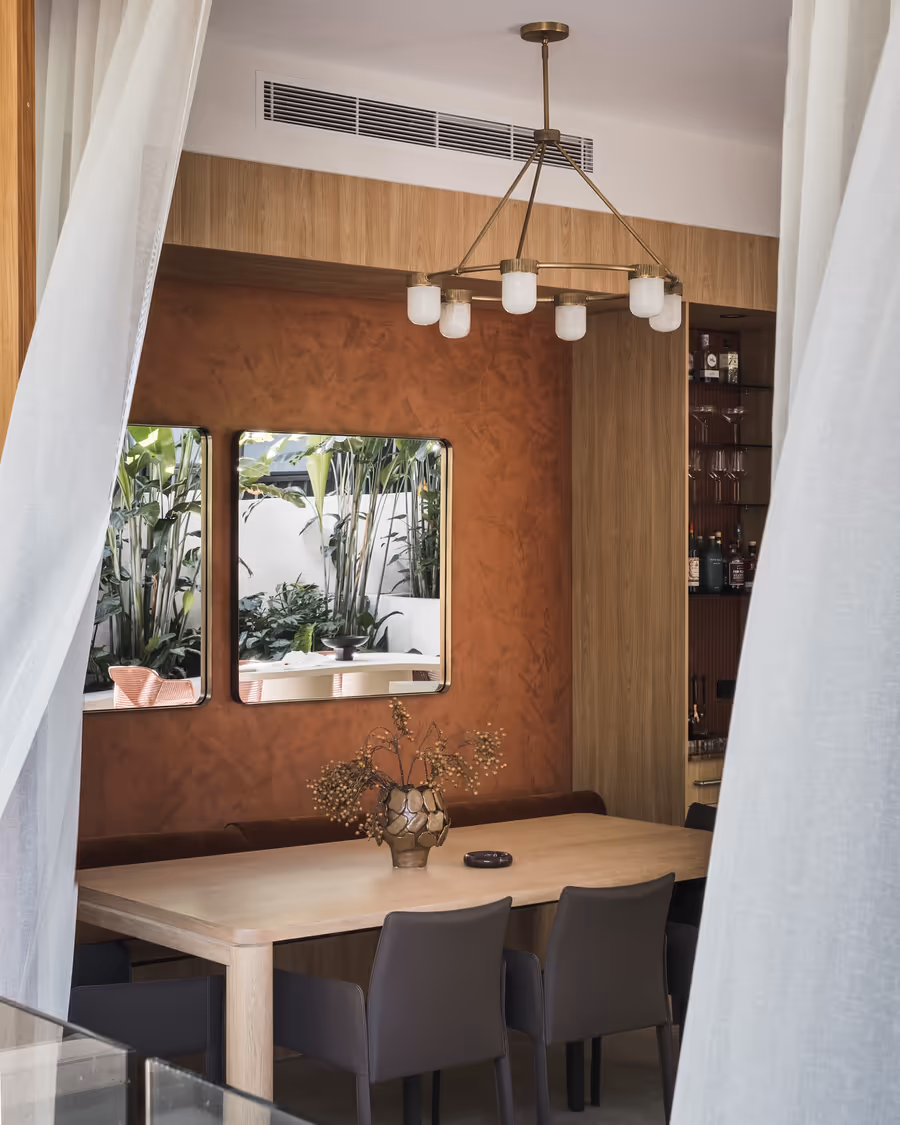Oak dining table under a globe chandelier, against the rust limewashed wall