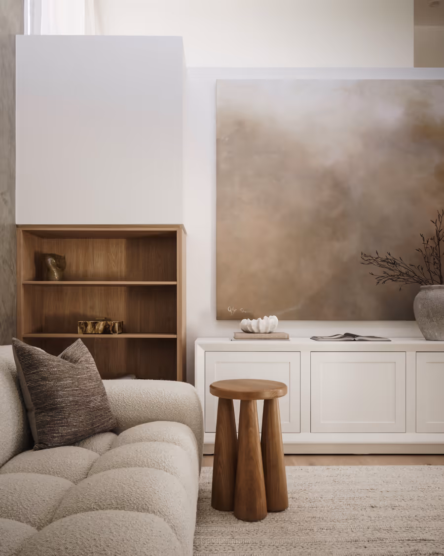 Boucle sofa and a timber stool beside white joinery, below a soft abstract canvas