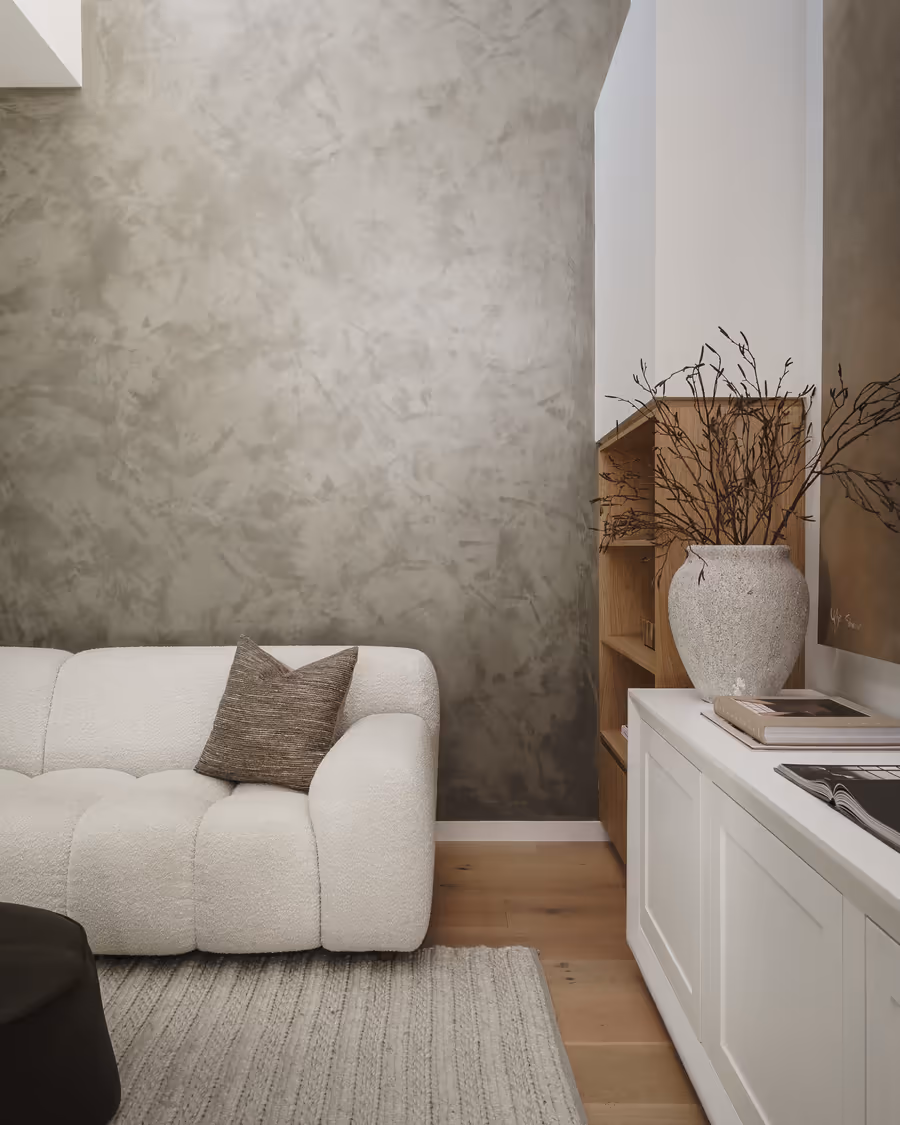 Boucle armchair against a limewashed wall, beside shelving and a tall stone vase