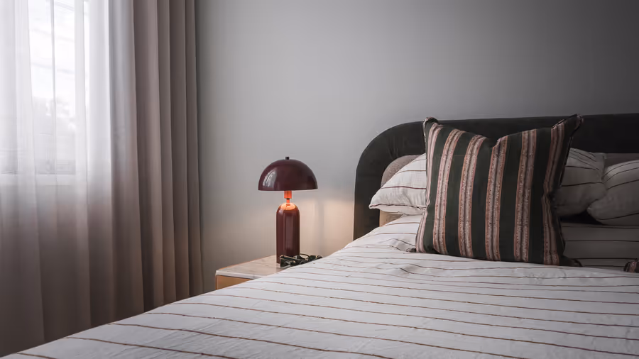 Striped cushions and a red mushroom lamp on the bed, sheers drawn at the window