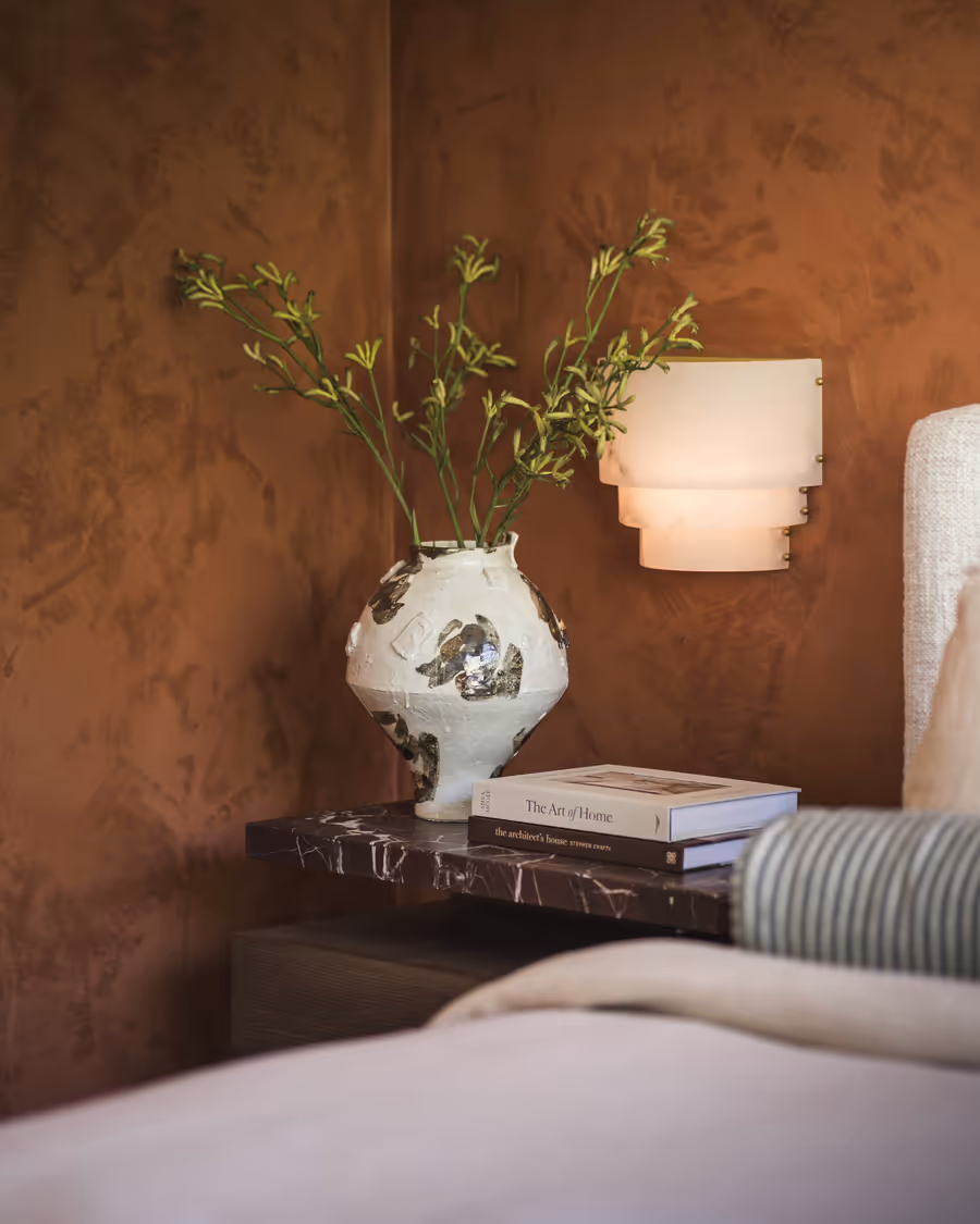 Kangaroo paw in a rough-glazed vase on a marble bedside, against the rust wall