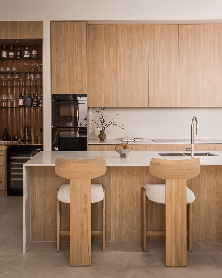 Oak kitchen with sculptural stools at the island, bar shelving behind