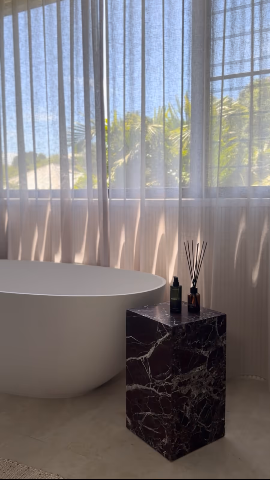 Freestanding bath beside a dark marble plinth, sheers filtering the courtyard light