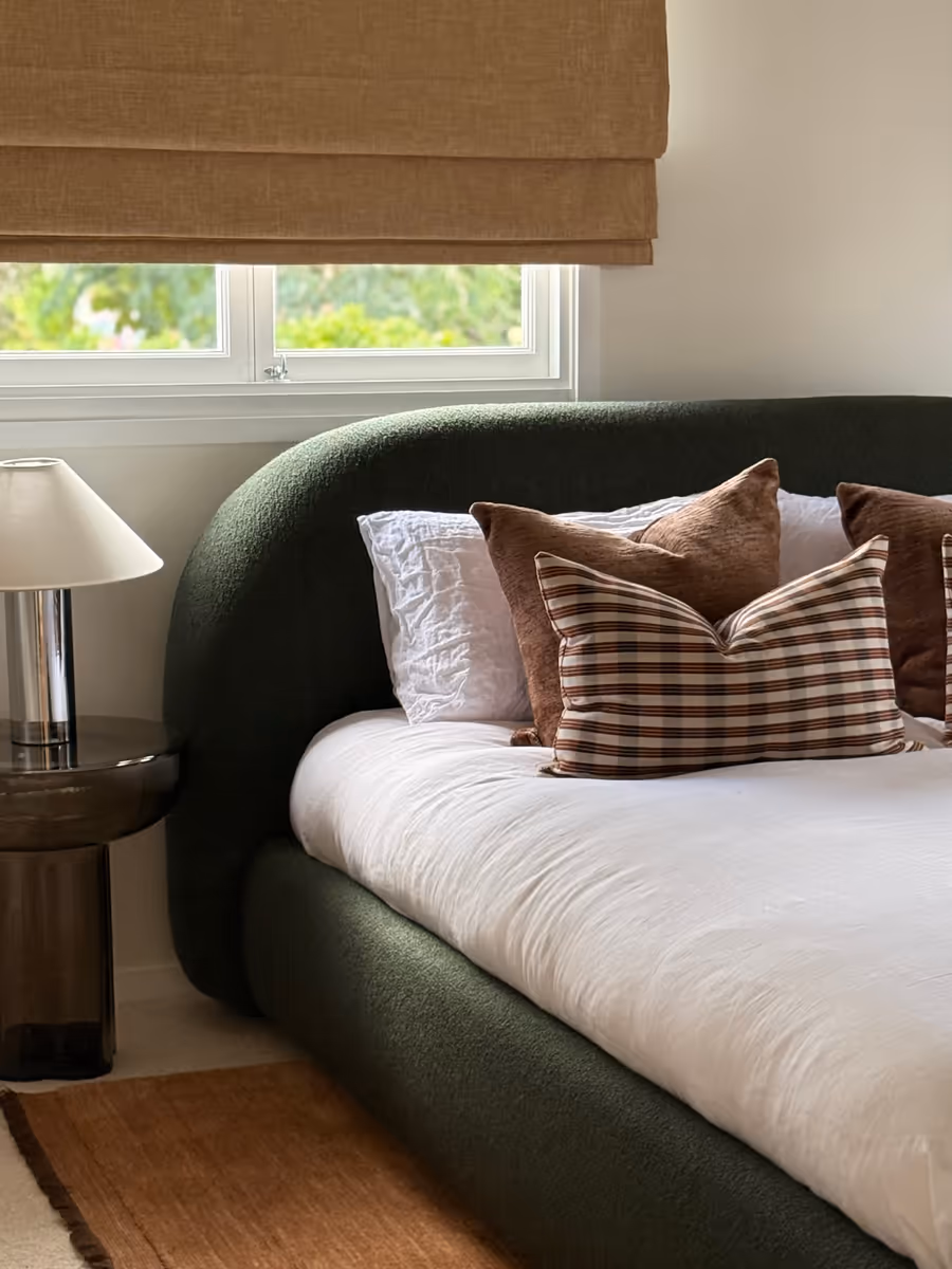 Dark green boucle bedhead with check and rust cushions, under a jute roman blind