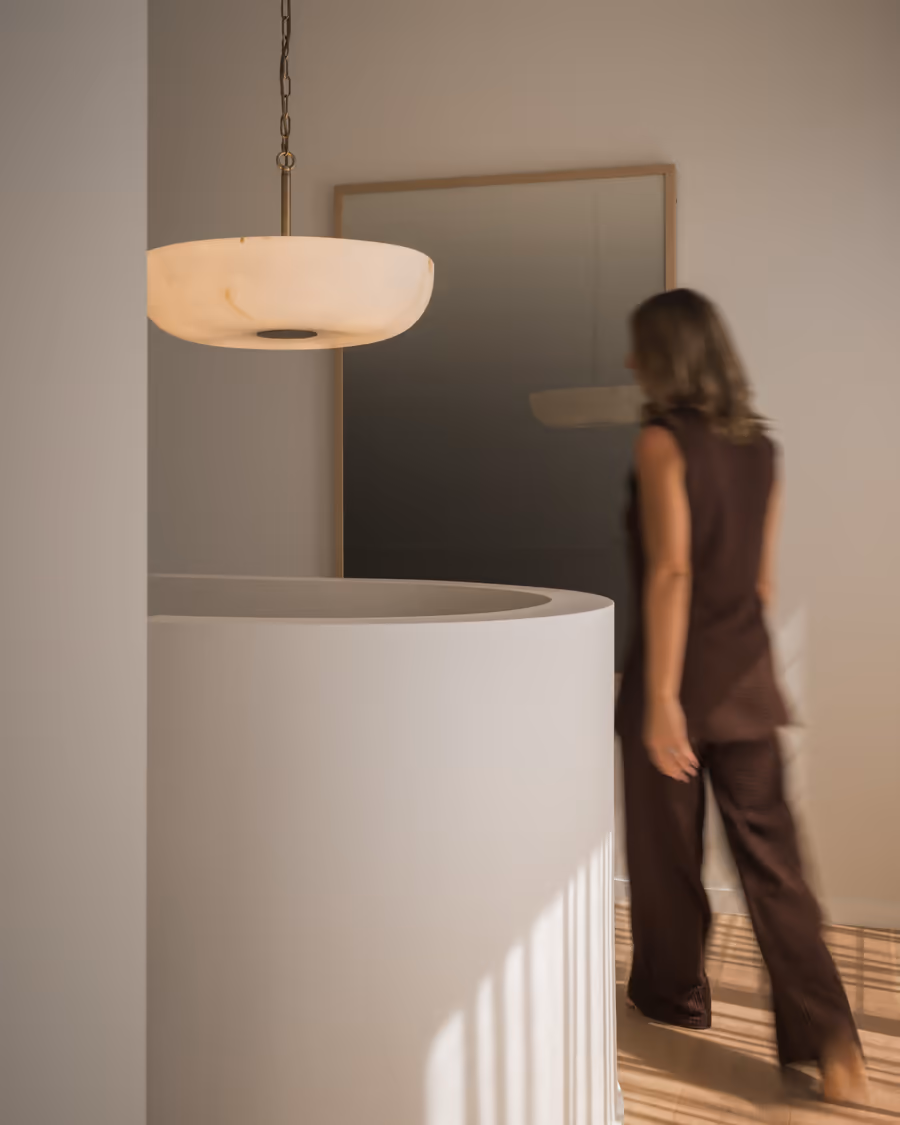 Curved rendered wall below an alabaster pendant, a woman walking past
