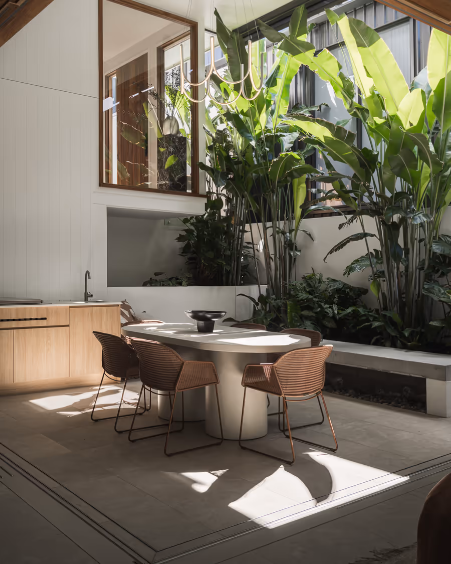 Outdoor dining table and woven chairs beside the planted courtyard
