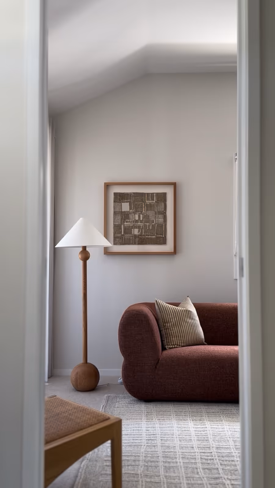 View through the doorway to a burgundy boucle sofa and a turned timber floor lamp