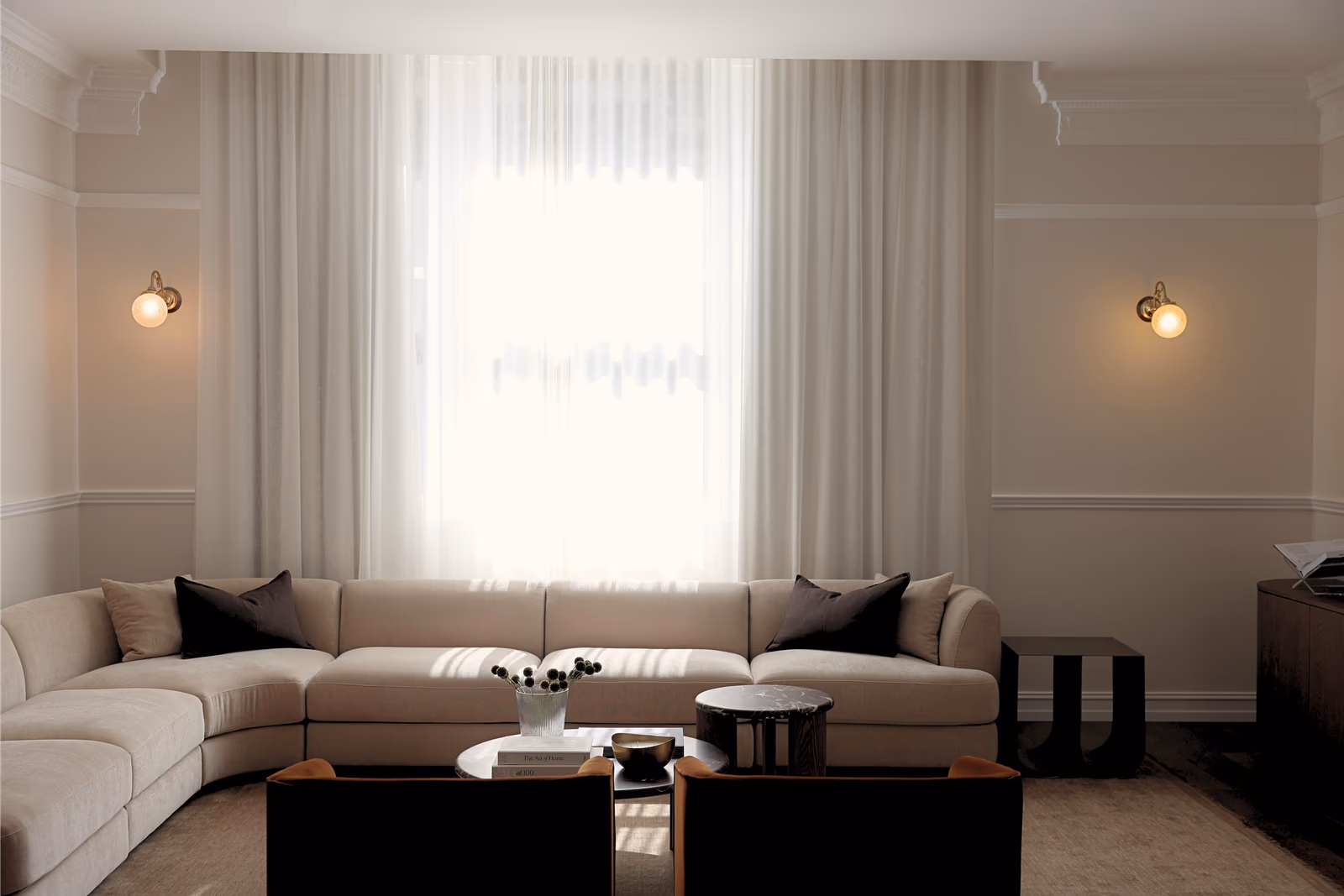 Cream modular sofa below the window, flanked by brass wall lights in the panelled living room
