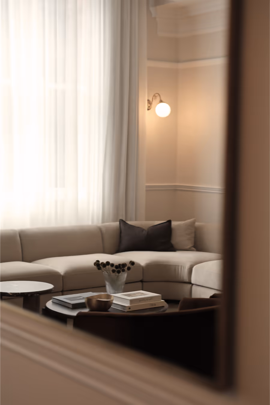 Living room reflected in a leaning mirror, a brass wall light above the sofa