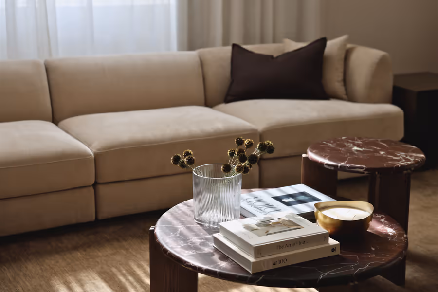 Cream modular sofa with a dark red marble coffee table holding books and a brass bowl