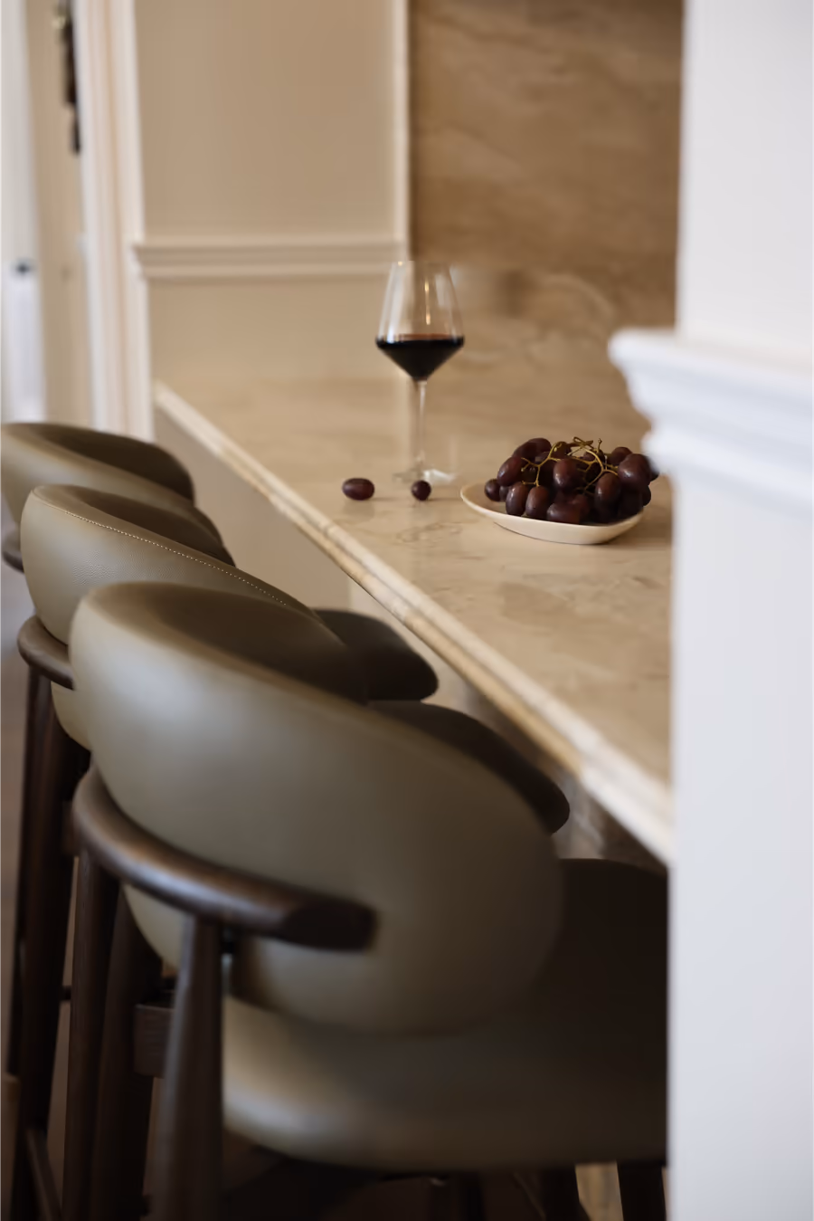 Olive leather stools along the stone breakfast bar, a glass of red wine on top