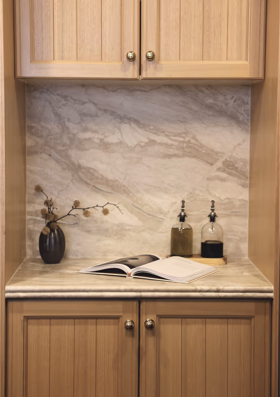 Timber pantry joinery with a marble splashback and an open book on the bench