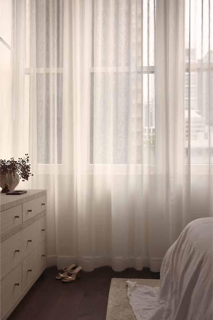 Cream chest of drawers by the sheer-curtained window, the bed beyond