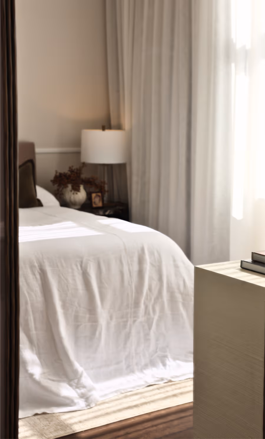 The bedroom reflected in a tall timber-framed mirror, lamp lit beside the bed