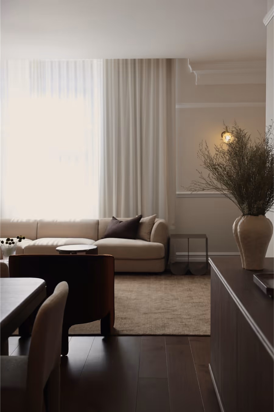 Cream sofa and dark timber dining table, with a tall urn of dried grasses