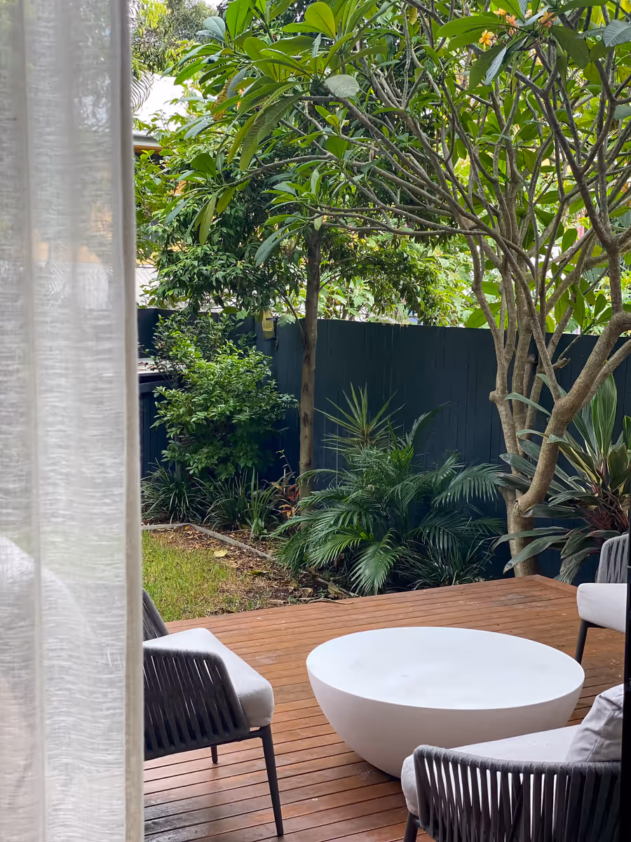 Woven chairs and a low table on the deck, looking into the frangipani garden