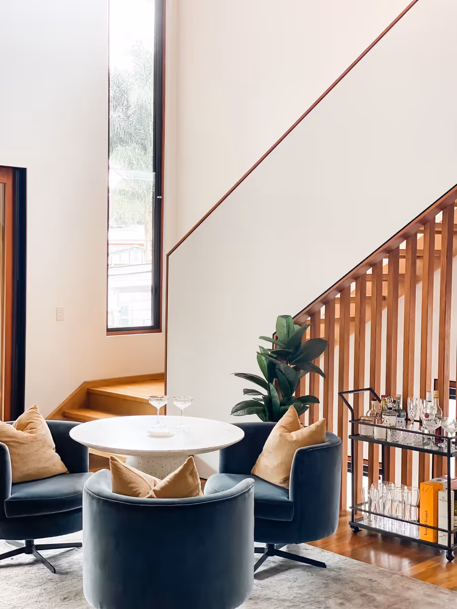 Navy swivel chairs around a white pedestal table, beside the timber stair and bar cart