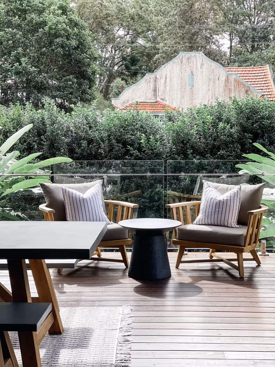 Timber chairs and a round table on the deck, looking out over the treetops